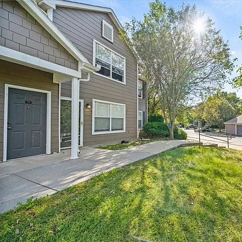 Charming apartment exterior with lush greenery and sunlit pathway leading to the front entrance, perfect for serene living.