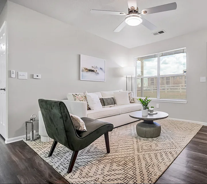 Bright and modern living room with stylish decor, featuring a cozy white sofa, elegant dark chair, and large window allowing natural light.