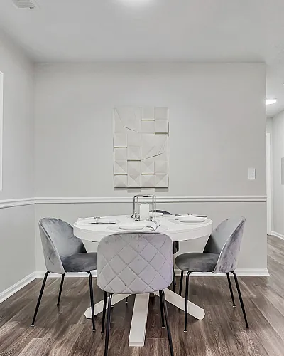 Chic dining area with modern gray chairs and a stylish round table, set for an inviting meal, accented by contemporary artwork on pristine walls.