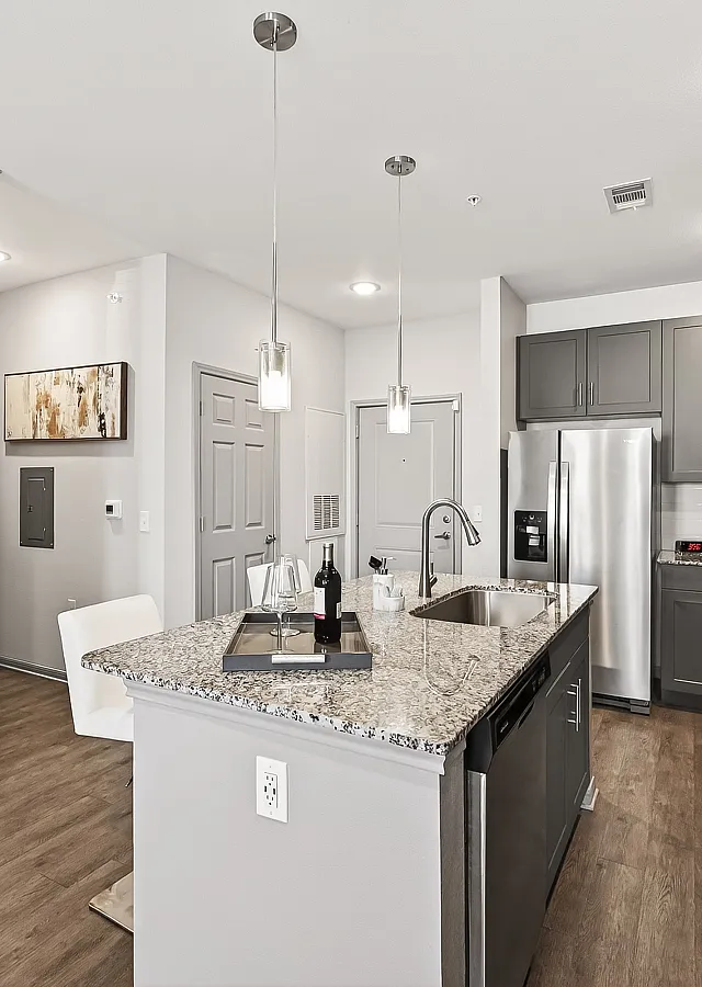 Modern kitchen with sleek granite countertops, gray cabinetry, and stainless steel appliances, featuring a stylish island with pendant lighting and elegant wood flooring.