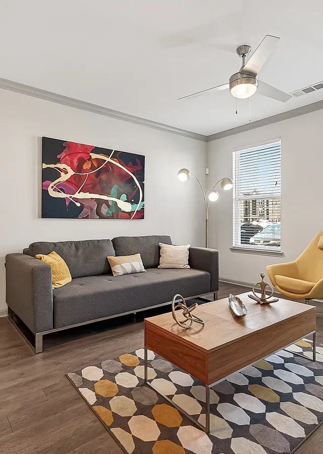 Contemporary living room featuring a sleek gray sofa, vibrant abstract artwork, and a stylish yellow armchair. Natural light floods through large windows, highlighting the modern decor and polished wooden flooring.