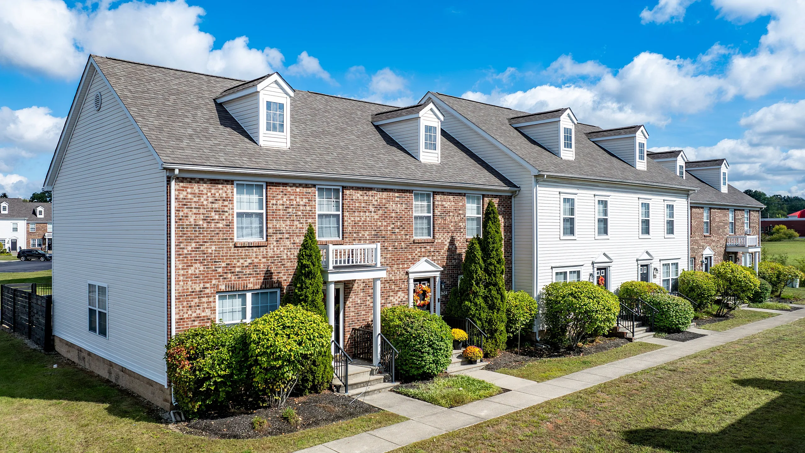 Charming row of townhouses with brick and siding exteriors, nestled in a lush green setting under a vibrant blue sky.