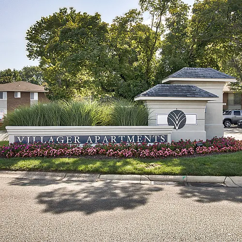 Charming entrance to Villager Apartments, surrounded by vibrant flowers and lush greenery, offering a serene and welcoming atmosphere.