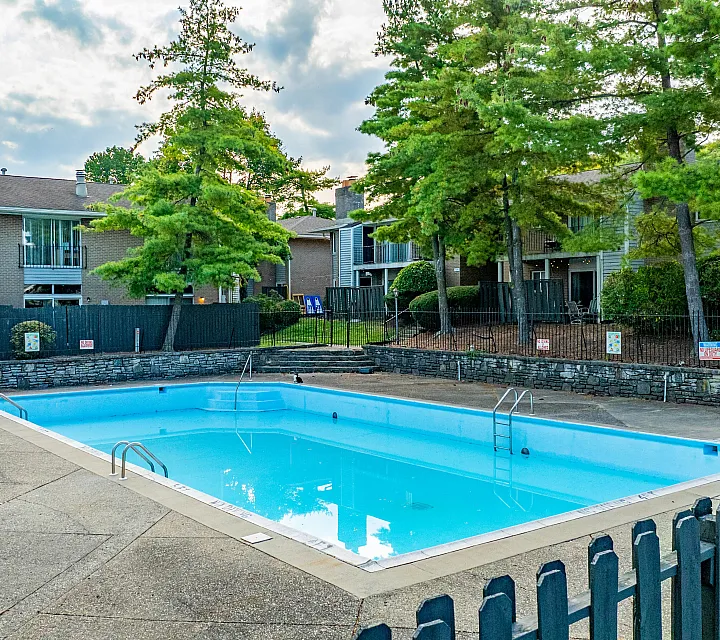 Inviting outdoor swimming pool surrounded by lush greenery and cozy apartment buildings, perfect for relaxation and leisure.