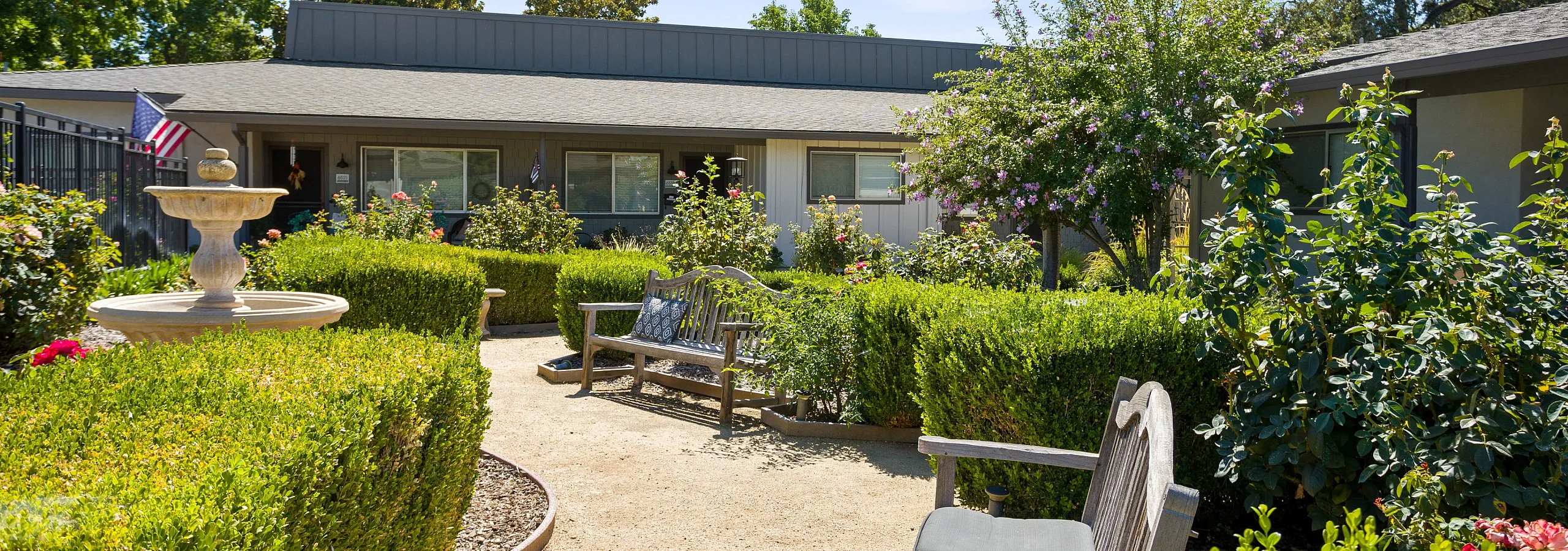 Charming garden courtyard with lush greenery, elegant fountain, and inviting benches, offering serene outdoor relaxation.