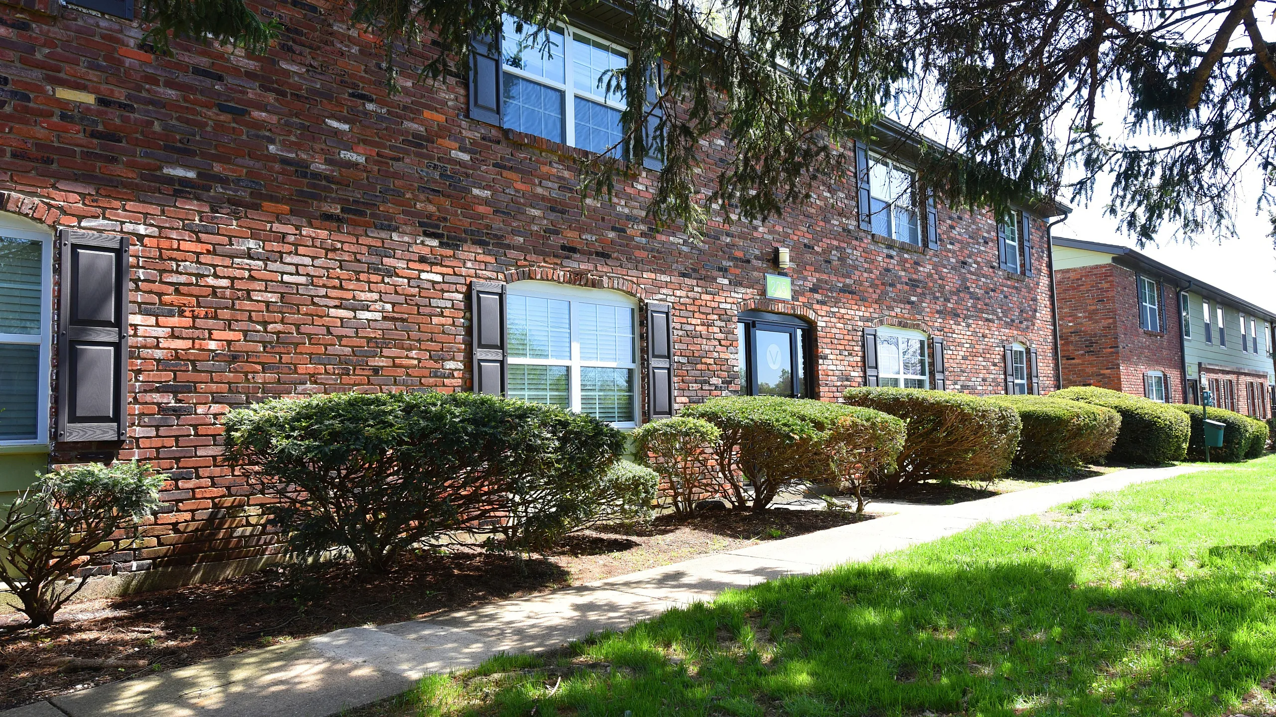 Charming brick apartment complex with landscaped bushes and vibrant green lawn, offering a welcoming and serene living environment.