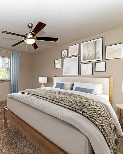 Chic bedroom featuring a plush bed, modern decor, and cozy seating area, bathed in natural light with stylish wall art and a ceiling fan.