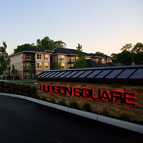 Charming Hudson Square apartments at dusk with lush landscaping and inviting entrance sign.