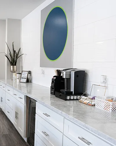 Inviting apartment interior with elegant white cabinetry, modern coffee station, and cozy blue velvet seating in a bright and spacious setting.
