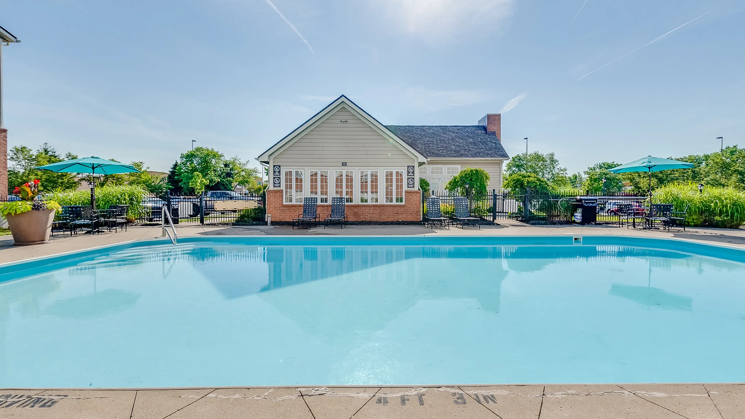 Inviting outdoor pool area with a charming clubhouse under a bright blue sky, perfect for relaxation and social gatherings.