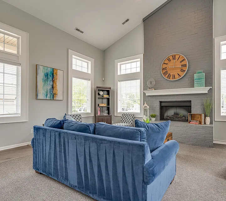 Inviting living room with elegant gray brick fireplace, oversized blue sofa, large windows, and stylish decor.