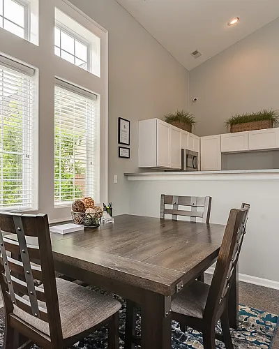 Bright dining area with large windows, elegant wooden table, and modern kitchen design offering natural light and a spacious feel.