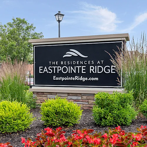 Modern and inviting sign for The Residences at Eastpointe Ridge, surrounded by vibrant landscaping and clear blue skies.