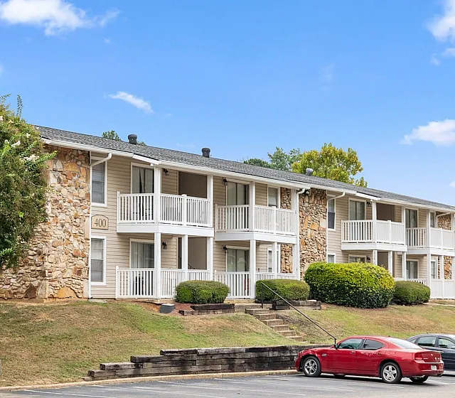 Charming apartment building with stone facade and inviting balconies, surrounded by lush greenery, against a vibrant blue sky.