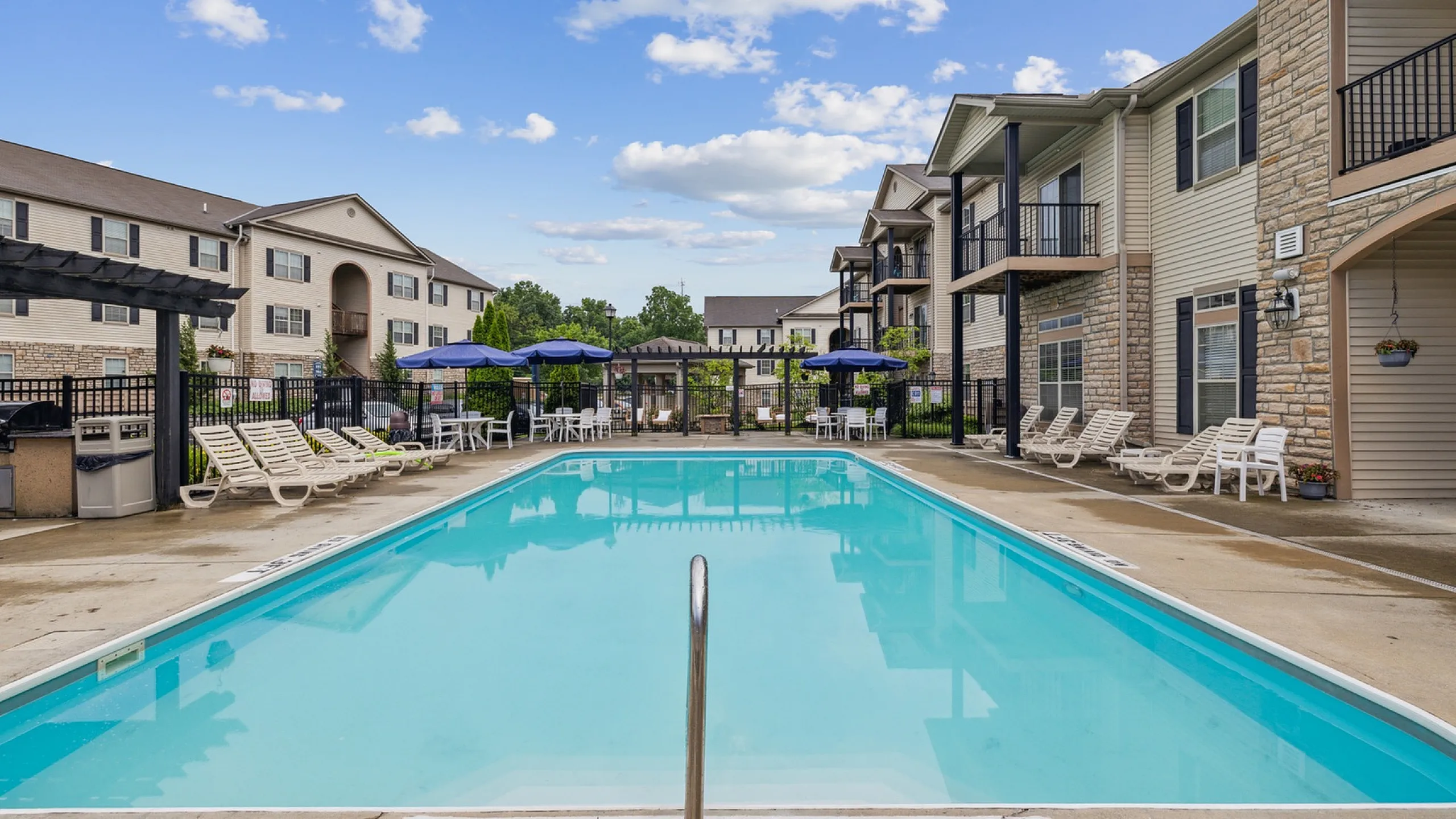 Inviting apartment complex featuring a sparkling pool surrounded by comfortable lounge chairs and shaded seating, perfect for relaxation and leisure.
