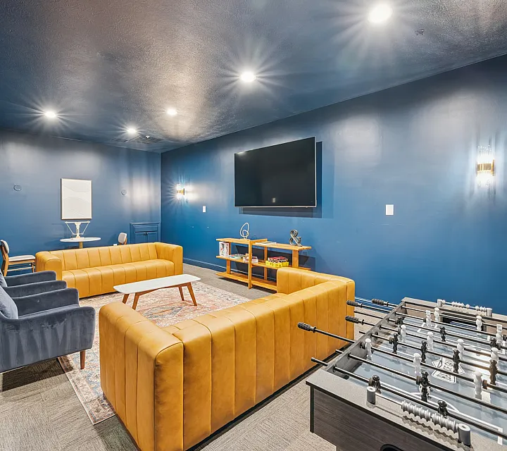 Chic entertainment room with vibrant blue walls, plush seating, a large flat-screen TV, and a foosball table, perfect for relaxation and social gatherings.