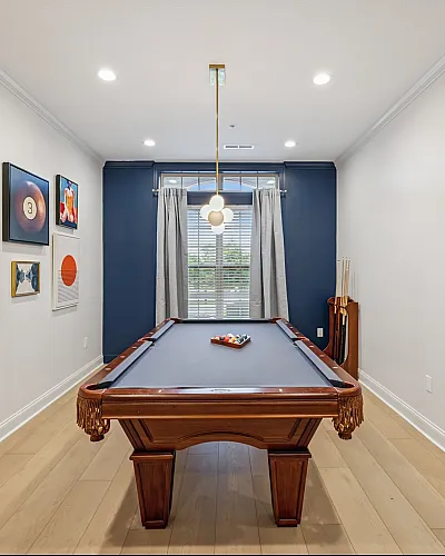 Elegant game room with a classic billiards table, vibrant wall art, and a modern light fixture, perfect for entertaining.