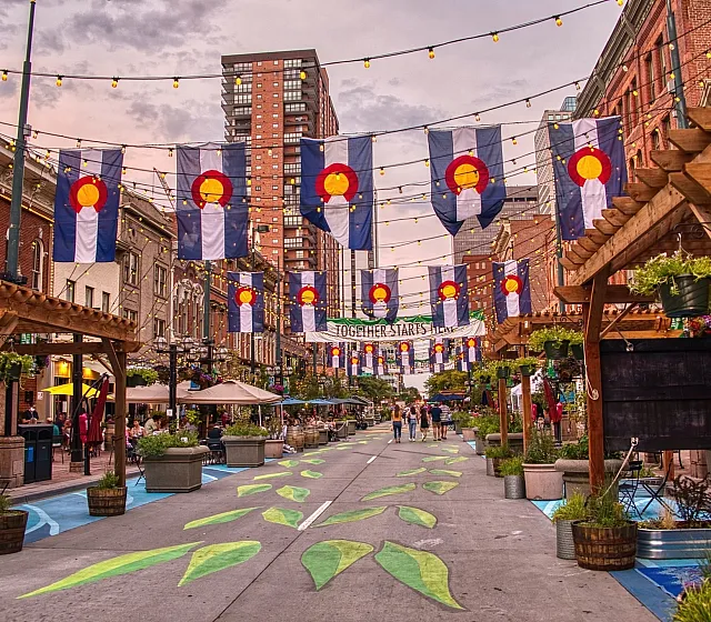 Vibrant urban street adorned with colorful flags, string lights, and bustling cafes, showcasing lively city ambiance.