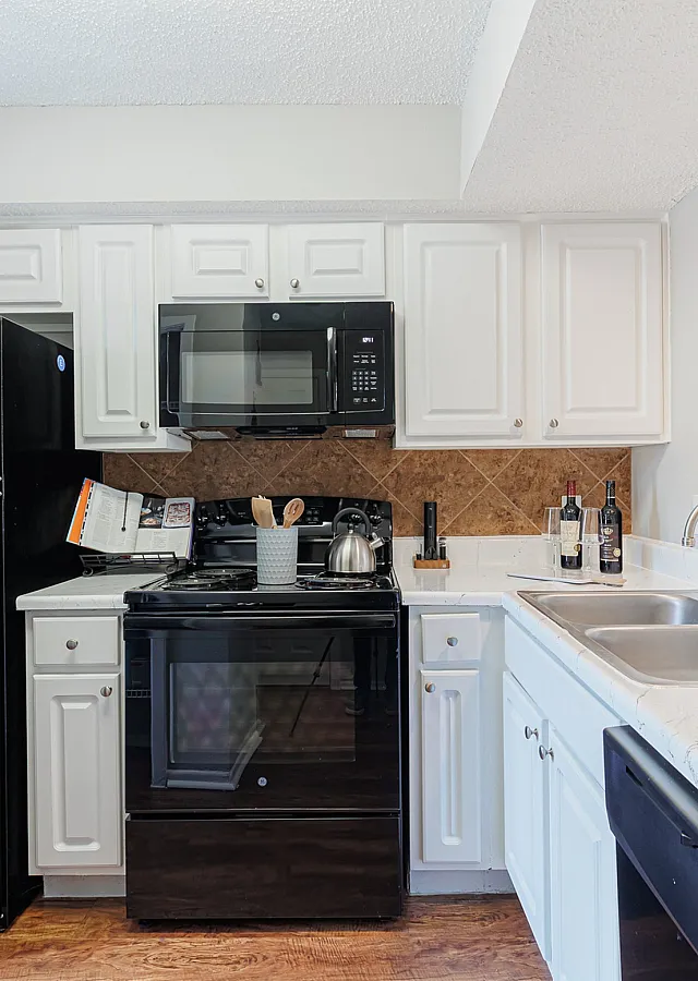 Charming kitchen featuring elegant white cabinetry, modern black appliances, and a spacious countertop perfect for culinary creativity.
