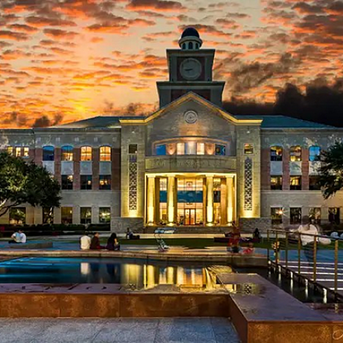 Majestic building with grand entrance and a clock tower set against a vibrant sunset sky, reflecting on a tranquil water feature.