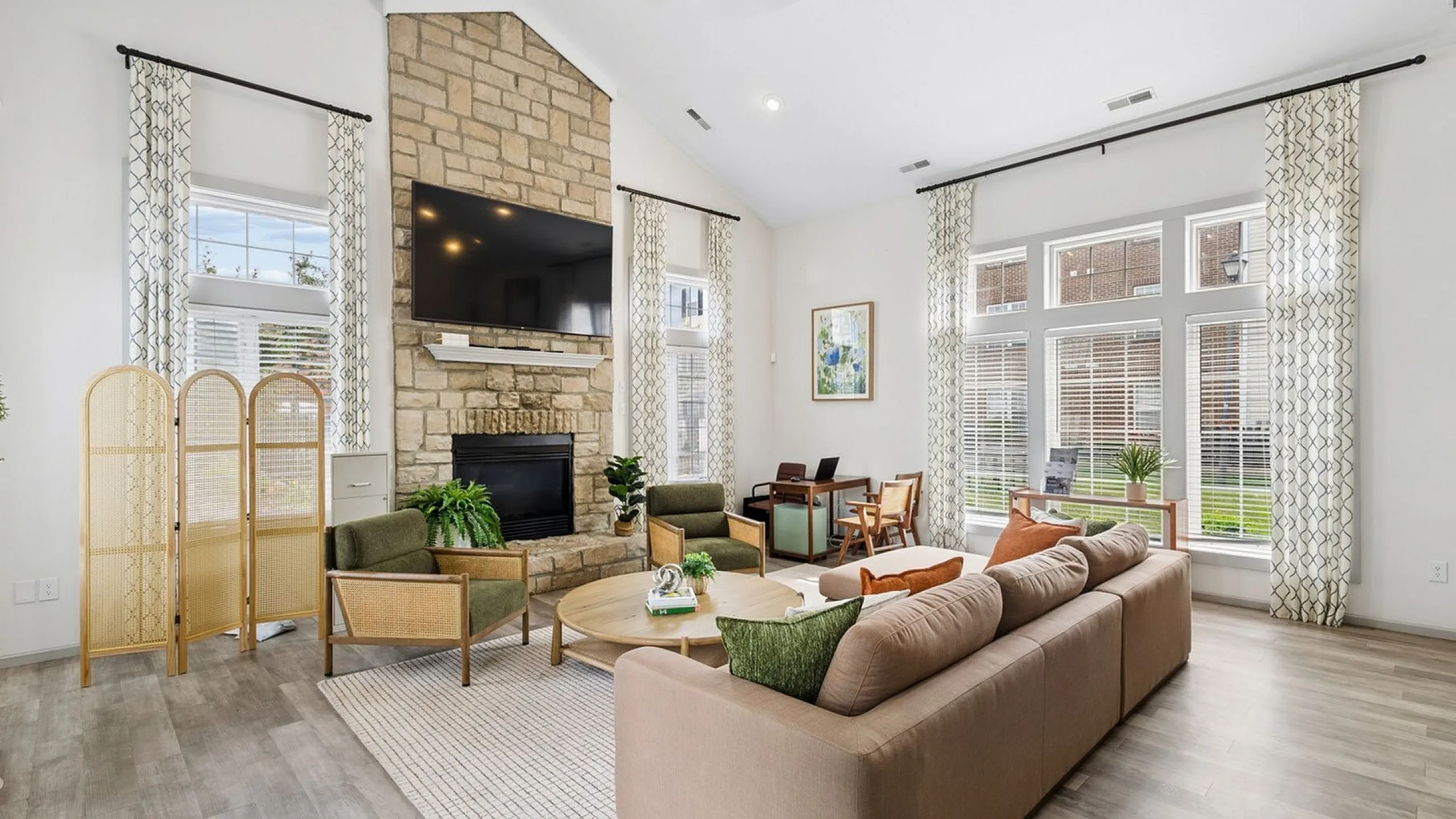 Elegant living room with high ceilings, stone fireplace, large TV, and ample natural light from tall windows.