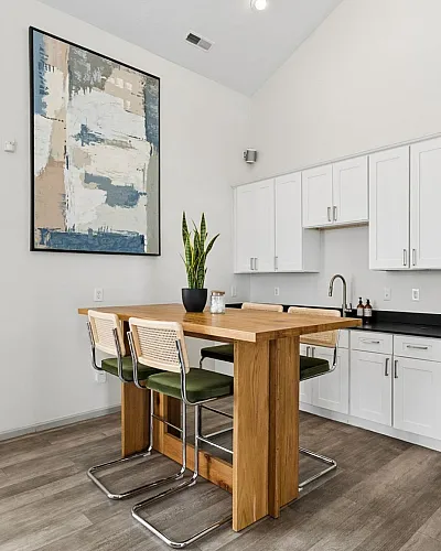Modern kitchen with sleek white cabinetry, a chic wooden dining table with stylish chairs, and contemporary abstract wall art.