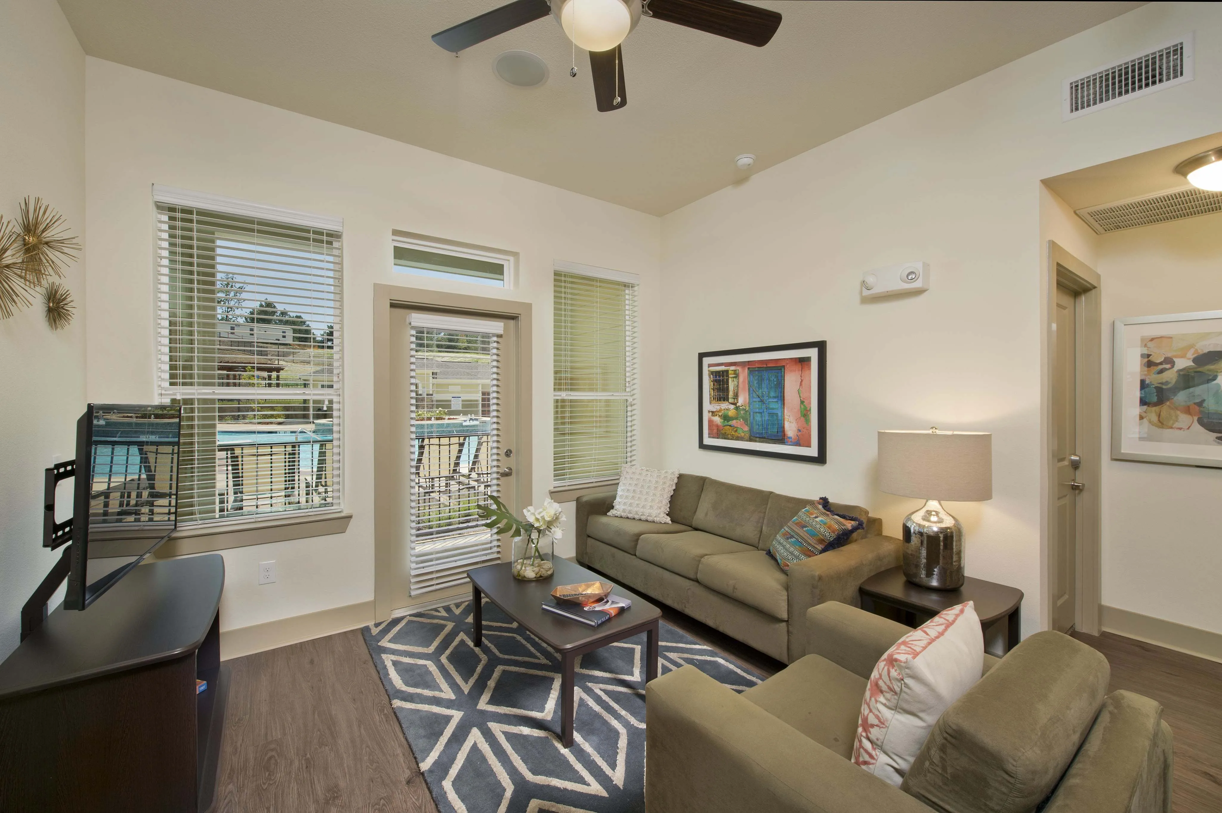 Chic living room featuring cozy beige sofas, elegant coffee table with a vase, vibrant wall art, and natural light streaming through large windows showcasing the pool view.