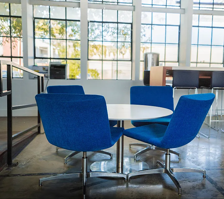 Modern dining area with blue chairs and a round table near large windows.
