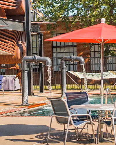 Chic urban pool area with industrial elements, featuring red umbrellas, lounge chairs, and a hammock.