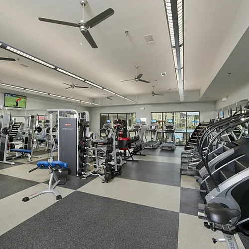 Modern fitness center with state-of-the-art equipment, treadmills, weight machines, and flat-screen TVs, offering a spacious workout environment.