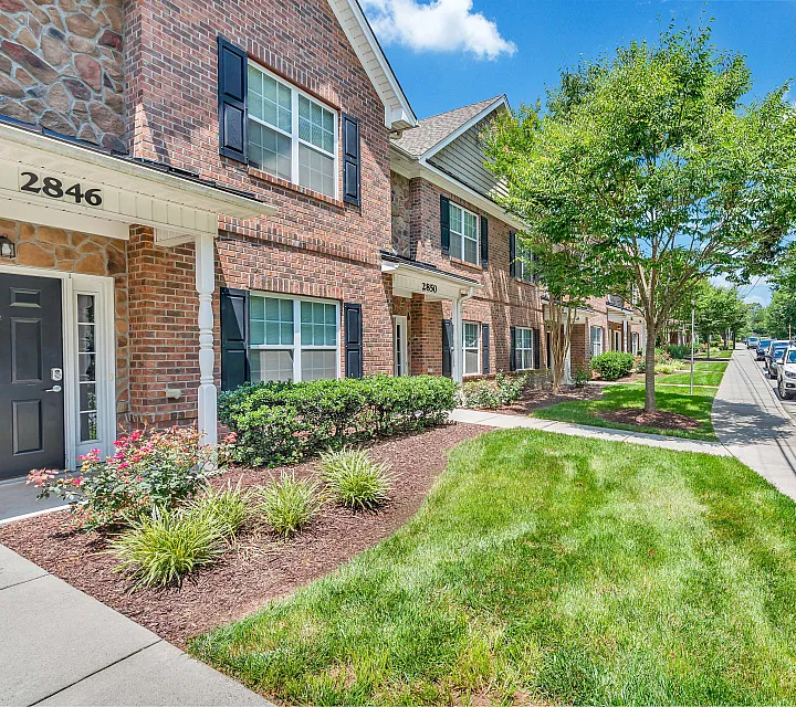 Charming brick townhouse with lush landscaping and inviting entrance on a sunny residential street, perfect for family living.