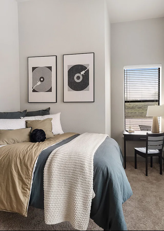 Cozy bedroom with modern decor, featuring stylish artwork, a comfortable bed by the window, and a compact workspace with a scenic outdoor view.
