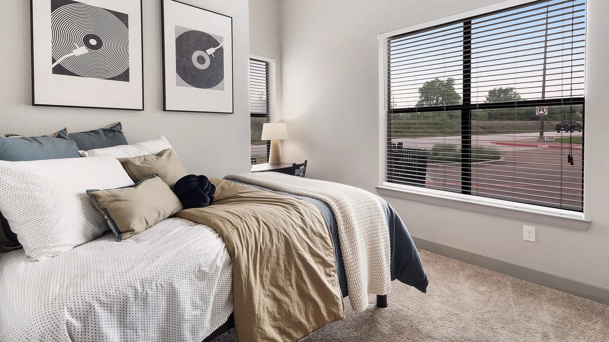 Inviting bedroom with stylish decor, featuring cozy bedding, modern artwork, and large window with scenic views.