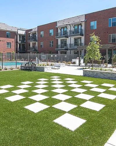 Modern apartment complex featuring a landscaped garden with a unique checkered walkway, and a sparkling pool area.