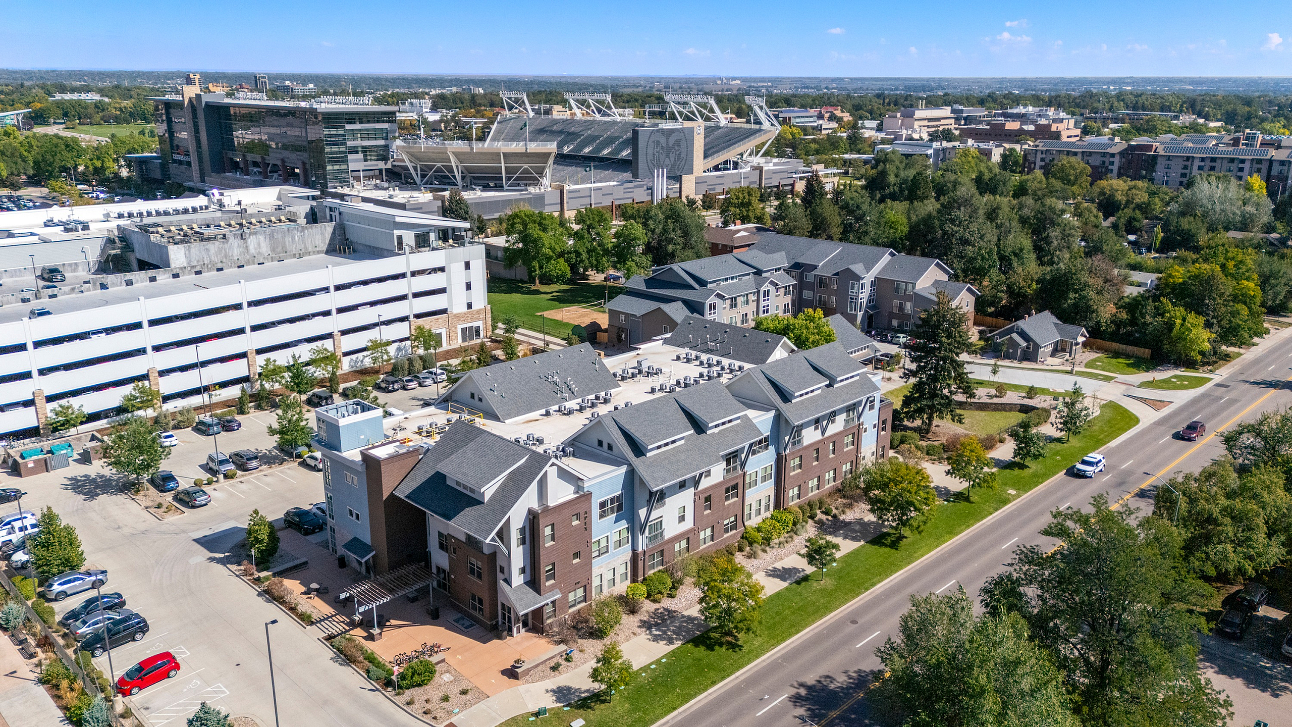Aerial view of modern residential apartments surrounded by lush greenery, a nearby stadium, and convenient parking, offering an ideal urban living experience.