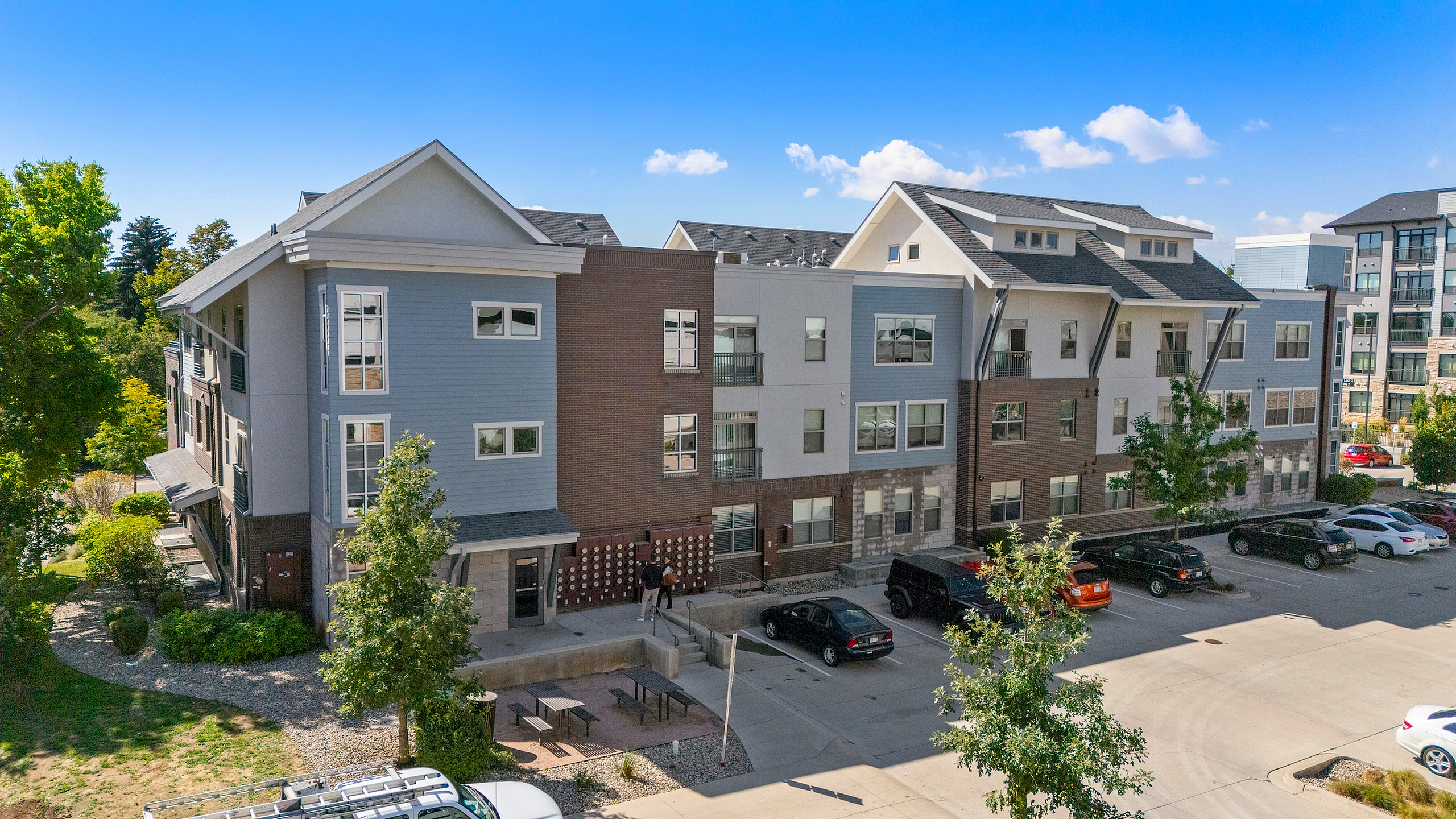 Charming multi-story apartment building with modern architecture, surrounded by lush greenery and ample parking.