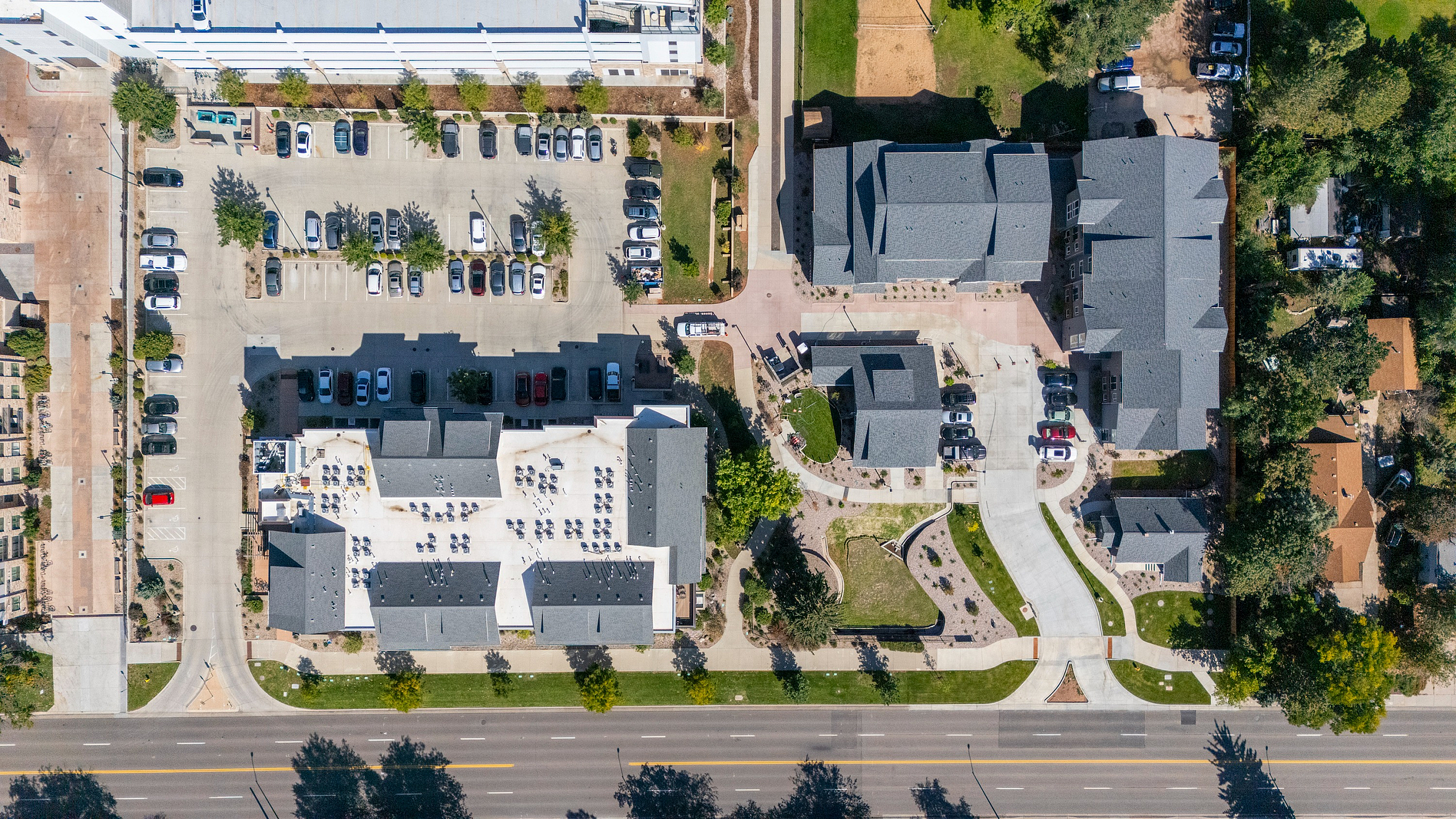 Aerial view of a modern apartment complex with spacious parking and lush greenery, offering a vibrant urban living experience.
