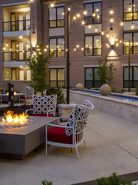 Charming outdoor patio with cozy fire pit seating, surrounded by stylish string lights and lush greenery, perfect for evening relaxation.