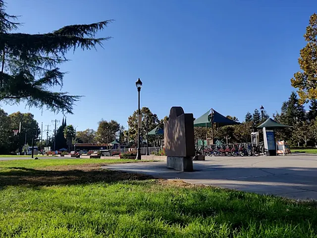 Charming park setting with lush greenery, modern playground, and serene pathways under a clear blue sky.