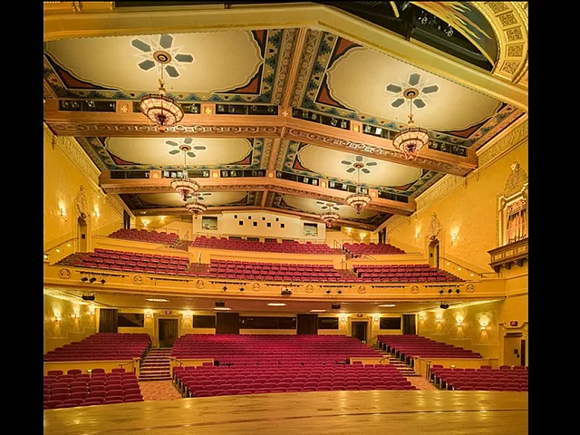 Elegant theater interior with ornate ceiling designs, plush red seating, and classic architectural elements.