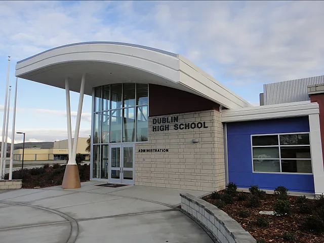 Modern architectural design of a high school's main entrance with sleek glass facade and dynamic roofing.