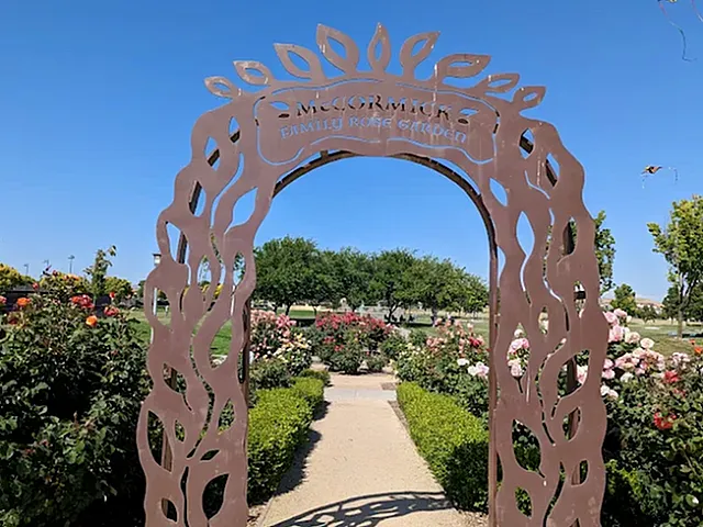 Charming garden entrance with elegant archway leading to vibrant rose garden under a clear blue sky.