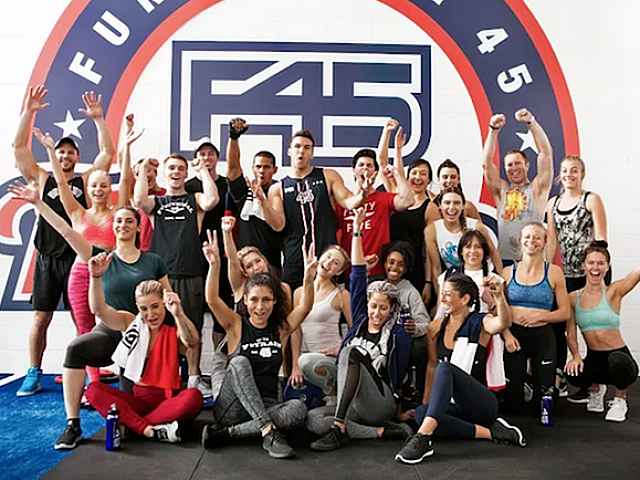 Vibrant fitness group celebrating in front of a bold F45 logo, showcasing teamwork and energy.
