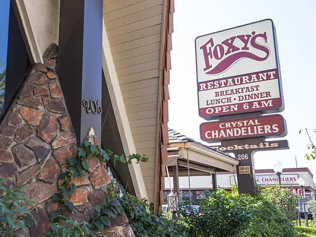 Inviting exterior of a restaurant with rustic stonework and lush greenery, featuring a vintage sign with bold lettering.