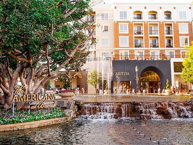 Vibrant outdoor scene at The Americana at Brand with lush greenery, a flowing fountain, and a stylish shopping experience.