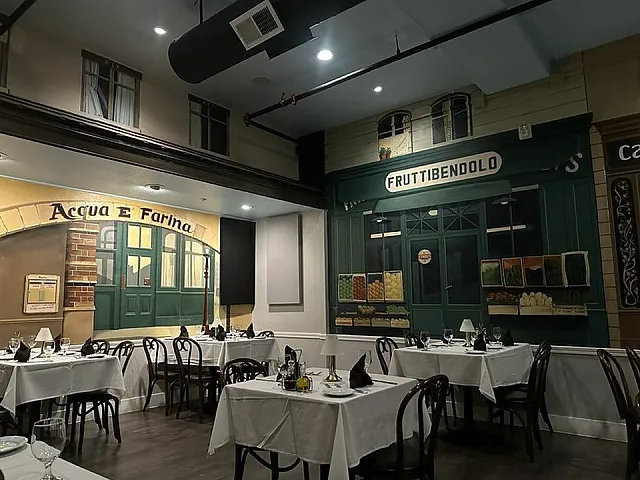 Charming Italian-themed restaurant interior featuring elegant wooden chairs, white tablecloths, and vibrant wall murals of classic storefronts.