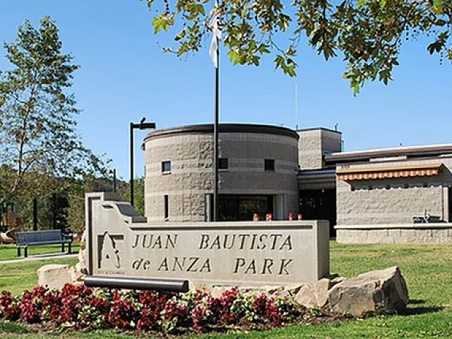 Charming view of Juan Bautista de Anza Park with lush greenery and modern architectural building.