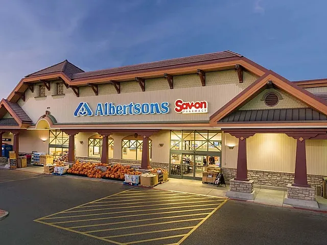 Charming Albertsons storefront at dusk with warm lighting and inviting entrance showcasing vibrant pumpkins and convenience services.