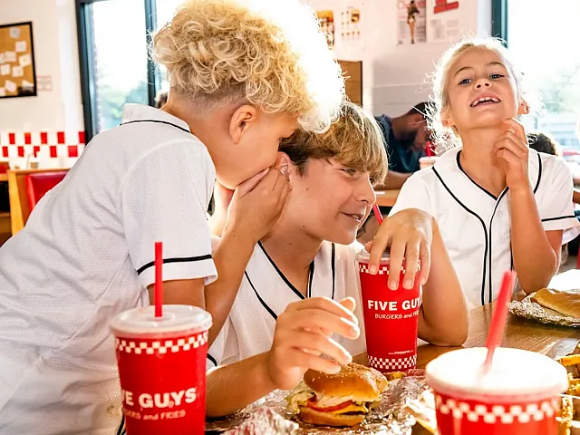 Joyful group of young friends enjoying burgers and shakes at a Five Guys restaurant, creating a vibrant and lively dining experience.