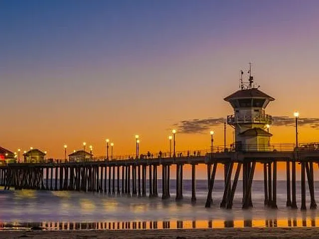 Sunset over a stunning pier, glowing lights illuminating the serene ocean and sky in vibrant hues.
